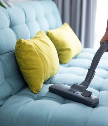 close up of man's hand cleaning couch using vacuum cleaner at home